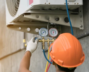 homme portant un casque de chantier orange qui répare l'unité extieure d'une PAC