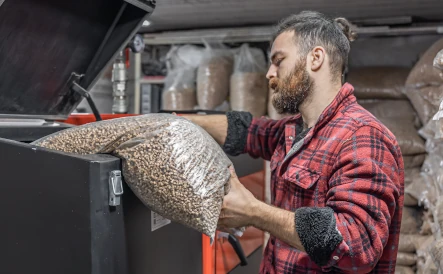 homme portant une chemise à carreaux rouge qui verse des pellets dans la chaudière à granulés
