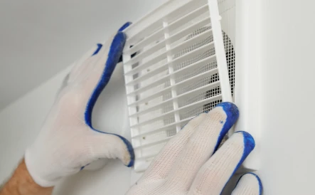 une personne qui démonte une VMC avec des gants bleu et blanc