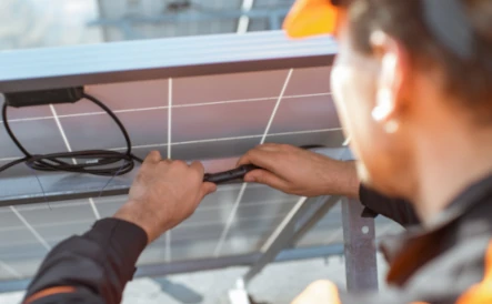 homme portant un gilet orange et un casque de chantier qui raccorde un panneau solaire