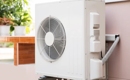 unité extérieure d'une pac air/eau sur un mur rose à coté d'une fenêtre avec des plantes