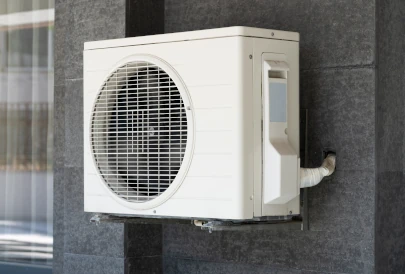 unité extérieure d'une pac sur un mur gris à coté d'une porte coulissante en verre