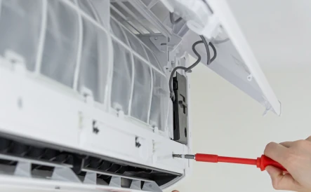 mains tenant un tournevis rouge qui répare une pompe à chaleur blanche