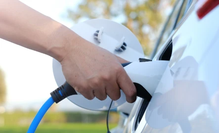 main qui recharge la batterie d'une voiture électrique blanche