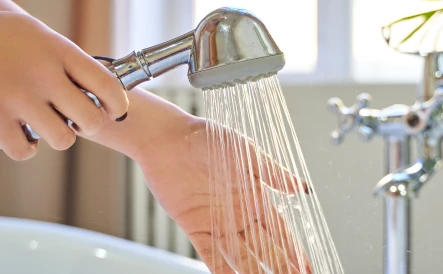 dame tenant le pommeau de douche et qui teste la température de l'eau 